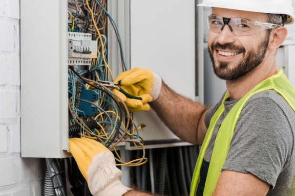 Smiling electrician wearing electrical personal protective equipment, using pliers to fix wires